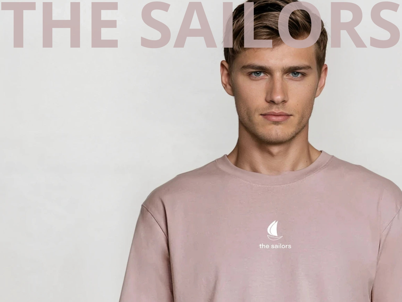 Man wearing a pink sweatshirt with 'The Sailors' logo on a light gray background