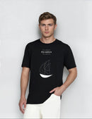 Man wearing a black t-shirt with a sailboat design on a plain background